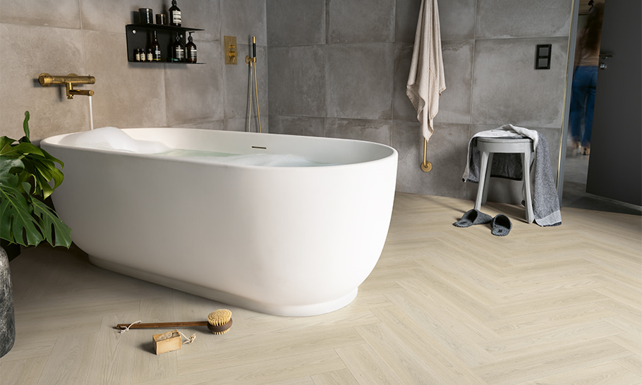 une salle de bain aux murs gris, avec une baignoire blanche et un sol vinyle beige clair en chevron